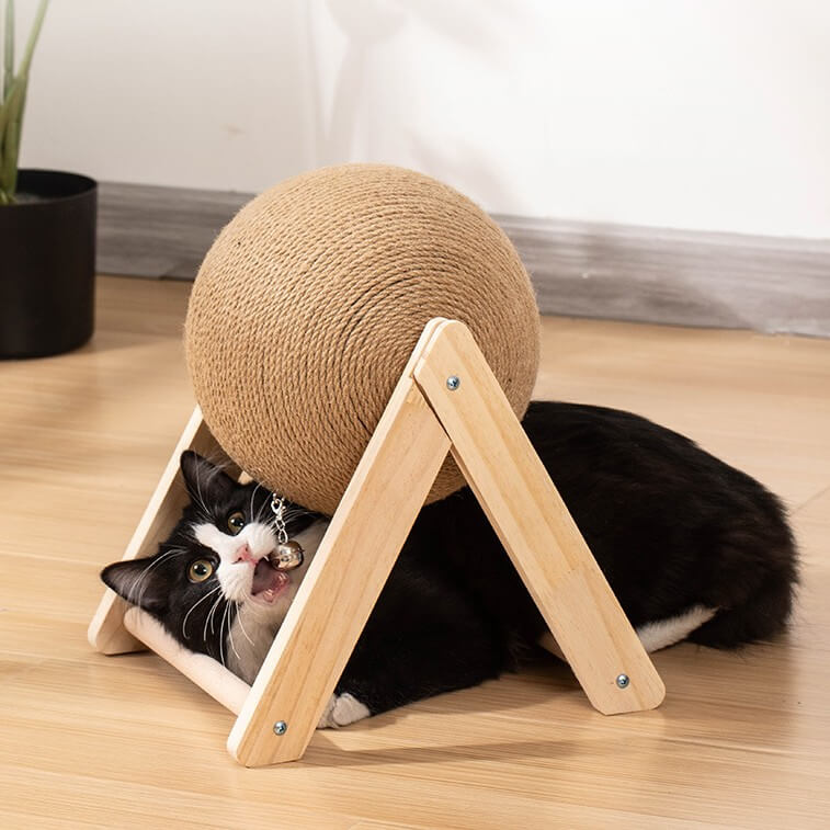 Cat playing with a spherical scratching post on a wooden floor.